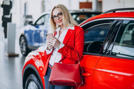 Téléchargez les photos : Femme d'affaires à la recherche d'un mobile automobile dans une salle d'exposition de voiture - en image libre de droit