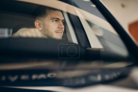 Foto de Hombre guapo sentado en el coche y probándolo - Imagen libre de derechos