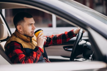 Téléchargez les photos : Portrait d'un bel homme assis en voiture et buvant du café - en image libre de droit