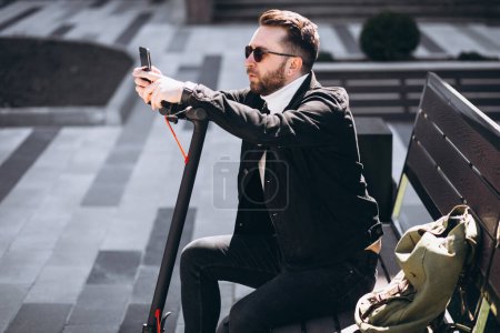 Téléchargez les photos : Bel homme sur scooter shopping en ligne sur le téléphone - en image libre de droit