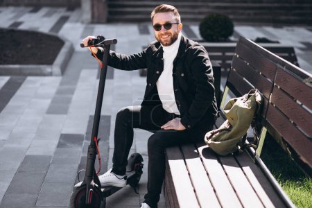 Téléchargez les photos : Jeune homme beau assis sur le banc dans le parc, se reposant d'une balade en scooter - en image libre de droit