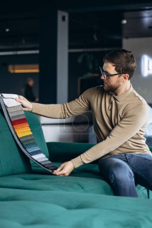 Téléchargez les photos : Homme assis sur le canapé dans le magasin de meubles choisir textile - en image libre de droit