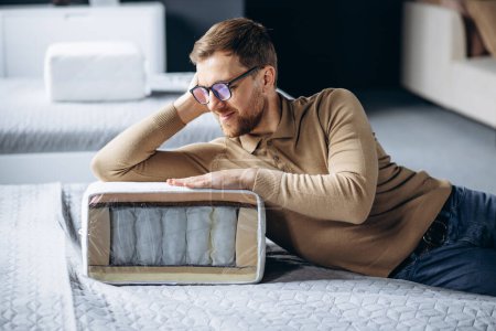 Téléchargez les photos : Homme bying nouveau lit avec oreiller orthopédique dans le magasin de meubles - en image libre de droit