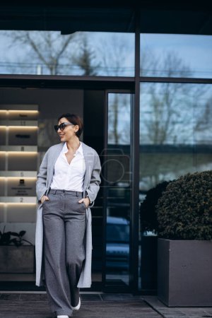 Téléchargez les photos : Belle femme d'affaires en manteau gris à l'extérieur du bâtiment de bureaux - en image libre de droit