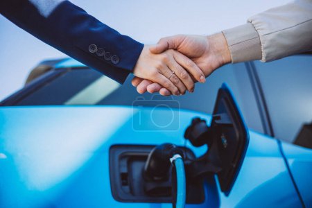 Photo for Man and woman shaking hands with a charging electric car on the background - Royalty Free Image