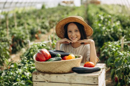 Photo for Young girl with basket full of vegetables standing in greenhouse - Royalty Free Image