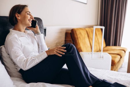 Photo for Business woman lying on a bed and talking on the phone in a hotel room - Royalty Free Image