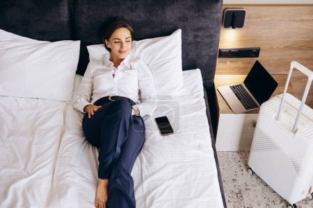 Photo for Business woman lying on a bed in a hotel room - Royalty Free Image