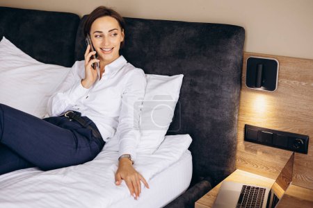 Foto de Mujer de negocios acostada en una cama y hablando por teléfono en una habitación de hotel - Imagen libre de derechos