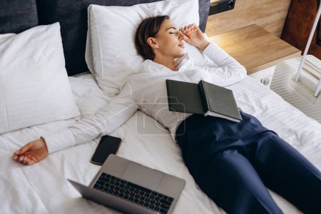 Photo for Business woman sleeping in a hotel room with laptop and phone lying on bed - Royalty Free Image