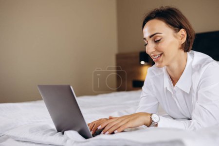 Photo for Business woman lying on bed and working on computer in a hotel room - Royalty Free Image