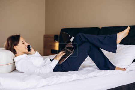 Téléchargez les photos : Femme d'affaires couchée dans son lit à l'hôtel et travaillant sur ordinateur - en image libre de droit