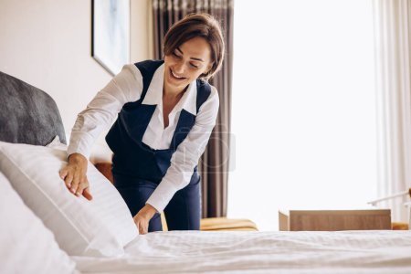 Téléchargez les photos : Femme femme de ménage préparant des draps et des oreillers dans la chambre d'hôtel - en image libre de droit