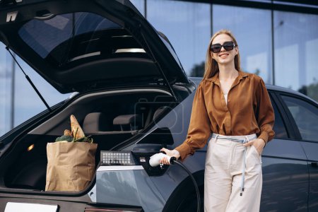 Photo for Woman with food shopping bags charging electric car - Royalty Free Image