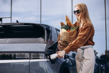 Photo for Woman doing grocery shopping while electric car charging - Royalty Free Image