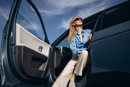 Photo for Woman sitting inside her electric car with open door - Royalty Free Image