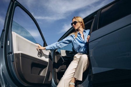 Téléchargez les photos : Femme assise à l'intérieur de sa voiture électrique avec porte ouverte - en image libre de droit