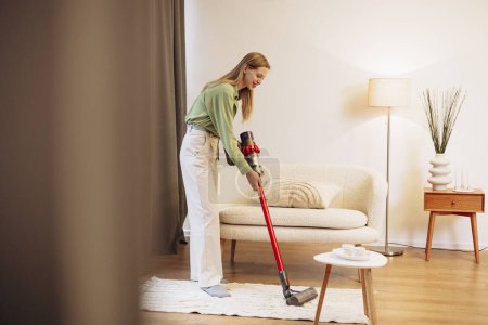 Photo for Woman doing house work and using wireless vacuum cleaner - Royalty Free Image