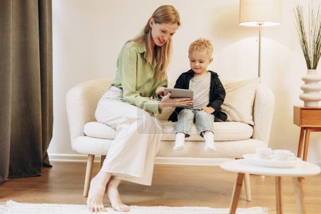 Téléchargez les photos : Femme assise avec son fils et utilisant une tablette jouant à des jeux - en image libre de droit