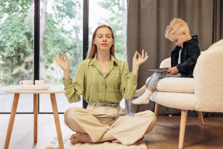 Photo for Woman meditating while her son playing video games on tablet - Royalty Free Image