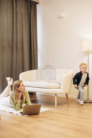 Foto de Mujer trabajando en la computadora mientras su hijo está jugando - Imagen libre de derechos