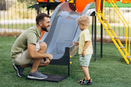 Téléchargez les photos : Père avec fils descendant la glissière sur le terrain de jeu - en image libre de droit