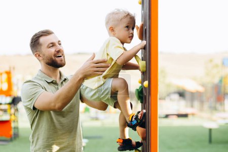 Téléchargez les photos : Garçon avec son père apprenant à grimper à l'aire de jeux - en image libre de droit
