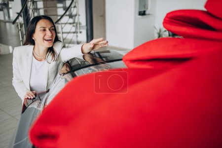 Téléchargez les photos : Femme heureuse par sa nouvelle voiture veut prendre de l'arc rouge de la voiture - en image libre de droit