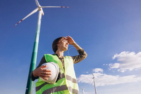 Téléchargez les photos : Femme ingénieur souriante et debout près des éoliennes - en image libre de droit