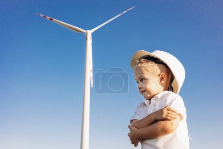 Foto de Lindo pequeño bou con casco de pie junto a las turbinas del molino de viento - Imagen libre de derechos