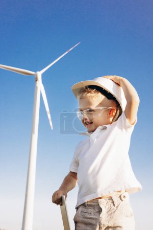 Photo for Cute little bou with helmet standing by the windmill turbines - Royalty Free Image