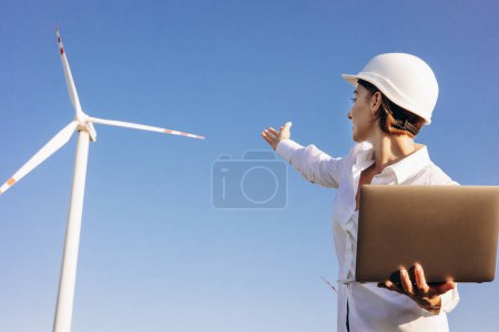 Foto de Mujer teniendo conferencia en línea en el portátil en el campo con turbinas de molino de viento - Imagen libre de derechos