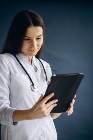 Téléchargez les photos : Jeune femme médecin en blouse de laboratoire tenant la tablette et vérifiant les analyses - en image libre de droit