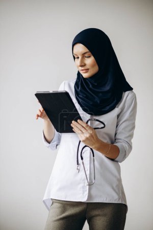Téléchargez les photos : Femme musulmane médecin isolé avec stéthoscope en utilisant une tablette - en image libre de droit