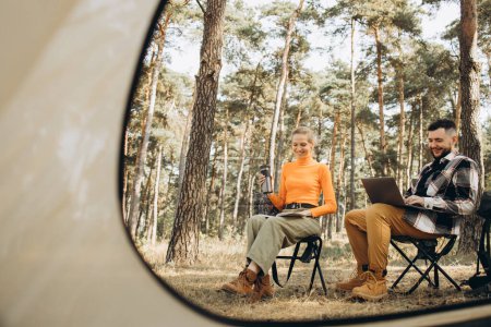 Photo for Couple travelers sitting by tent and working on computer - Royalty Free Image