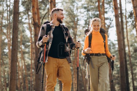 Téléchargez les photos : Couple randonnée avec sacs et bâtons de marche en forêt - en image libre de droit