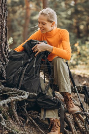 Téléchargez les photos : Femme voyageur regardant dans son sac dans la forêt près de l'arbre - en image libre de droit