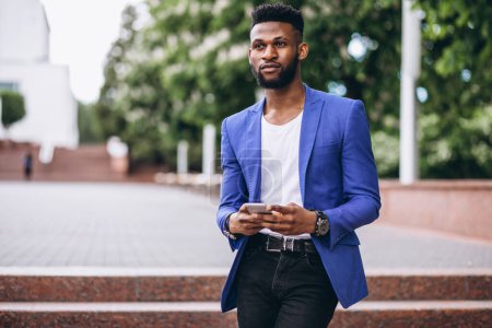 Téléchargez les photos : Africain américain en veste bleue en utilisant le téléphone - en image libre de droit
