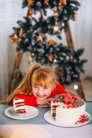 Photo for Little girl with red hair eating christmas cake by the christmas tree - Royalty Free Image