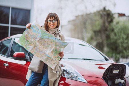 Foto de Mujer con mapa de viaje viajando en coche electro - Imagen libre de derechos