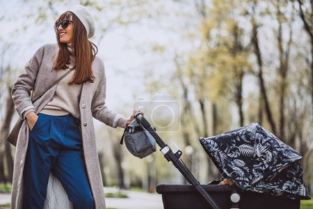 Photo for Young mother walking with baby carriage in park - Royalty Free Image