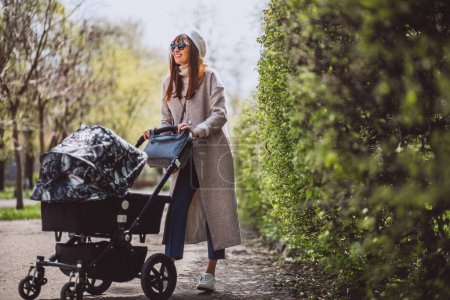 Téléchargez les photos : Jeune mère marchant avec la voiture de bébé dans le parc - en image libre de droit