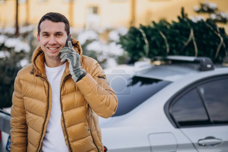 Foto de Hombre guapo hablando por teléfono junto al coche con árbol de Navidad en la parte superior - Imagen libre de derechos