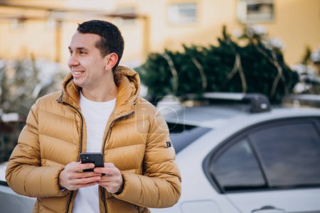 Téléchargez les photos : Bel homme parlant au téléphone près de la voiture avec arbre de Noël sur le dessus - en image libre de droit