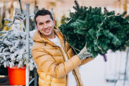 Photo for Handsome man choosing a christmas tree in a greenhouse - Royalty Free Image