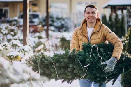 Téléchargez les photos : Beau homme choisissant un arbre de Noël dans une serre - en image libre de droit