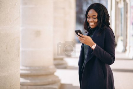 Foto de Chica estudiante afroamericana con teléfono por la universidad - Imagen libre de derechos