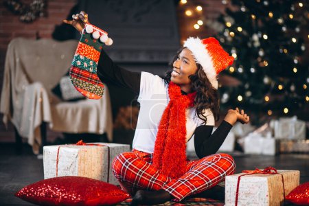 Téléchargez les photos : Femme afro-américaine tenant des cadeaux de Noël près de l'arbre de Noël - en image libre de droit