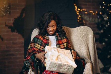 Téléchargez les photos : Femme afro-américaine assise sur une chaise et déballer des cadeaux de Noël - en image libre de droit