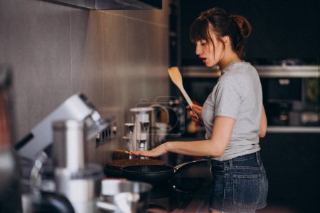Téléchargez les photos : Jeune femme préparant le petit déjeuner dans la cuisine le matin - en image libre de droit